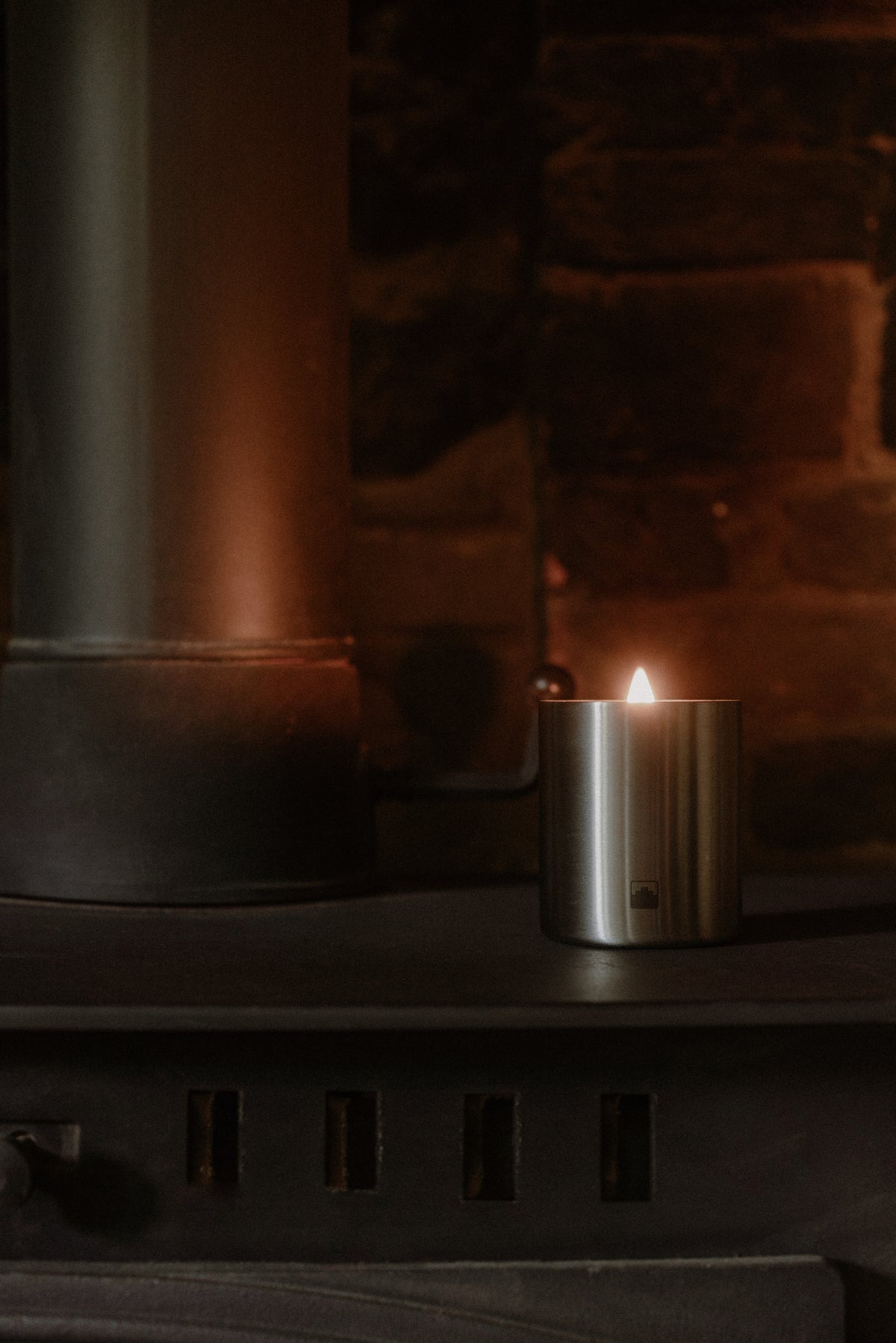 Candle in a metal holder next to a fireplace