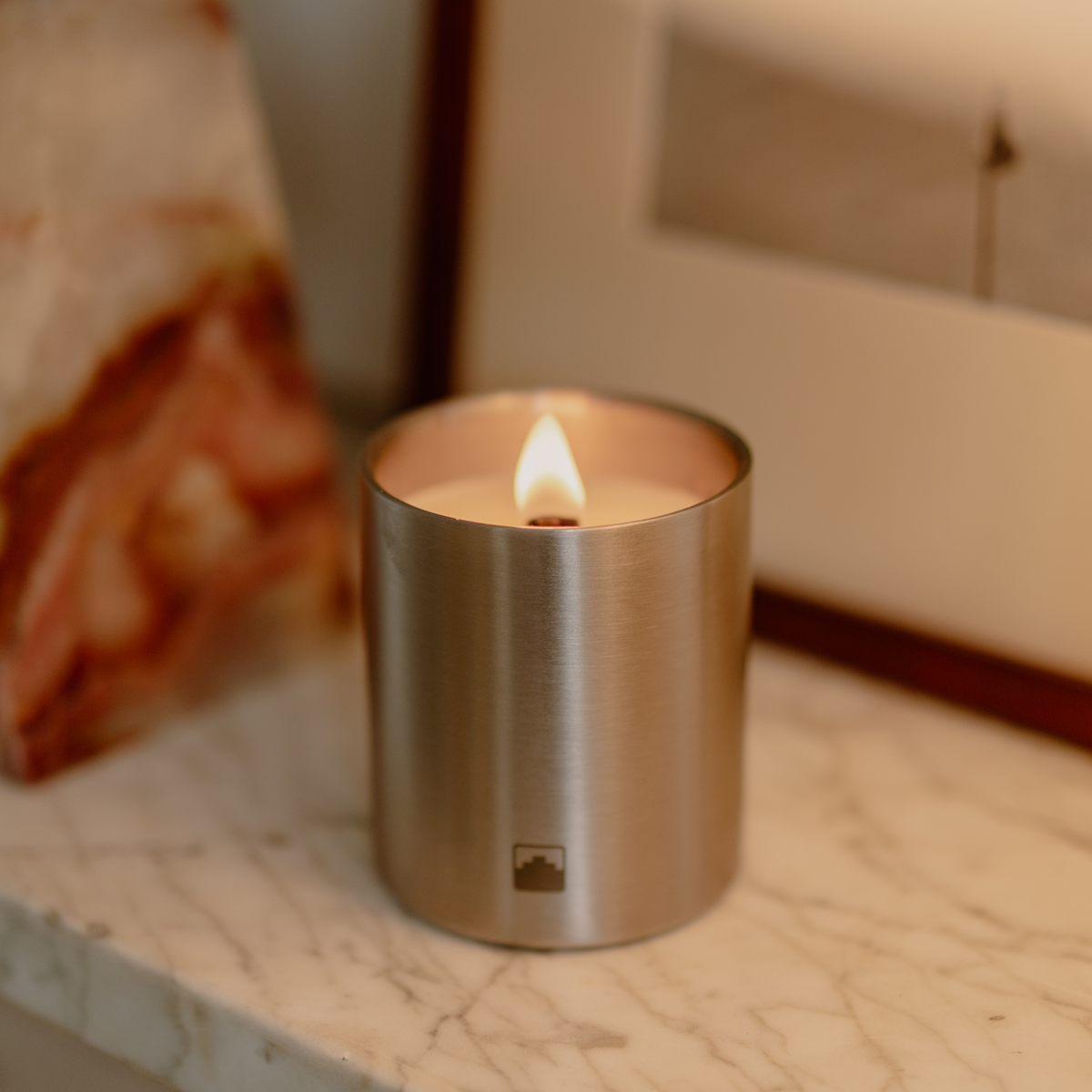 Candle in a stainless steel container on a marble surface with a blurred background