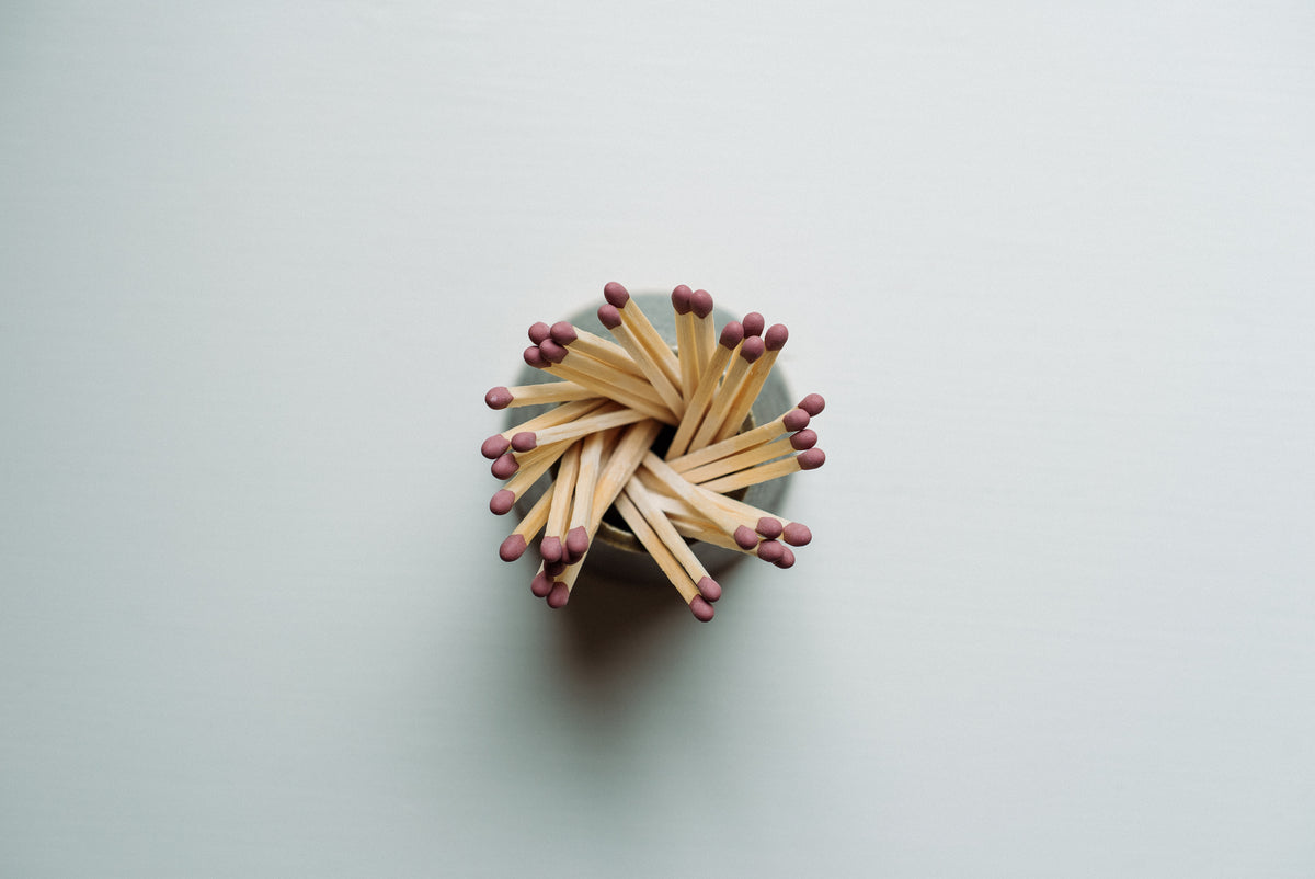 A small bundle of wooden matchsticks with red tips arranged in a circular starburst pattern on a plain light gray background.