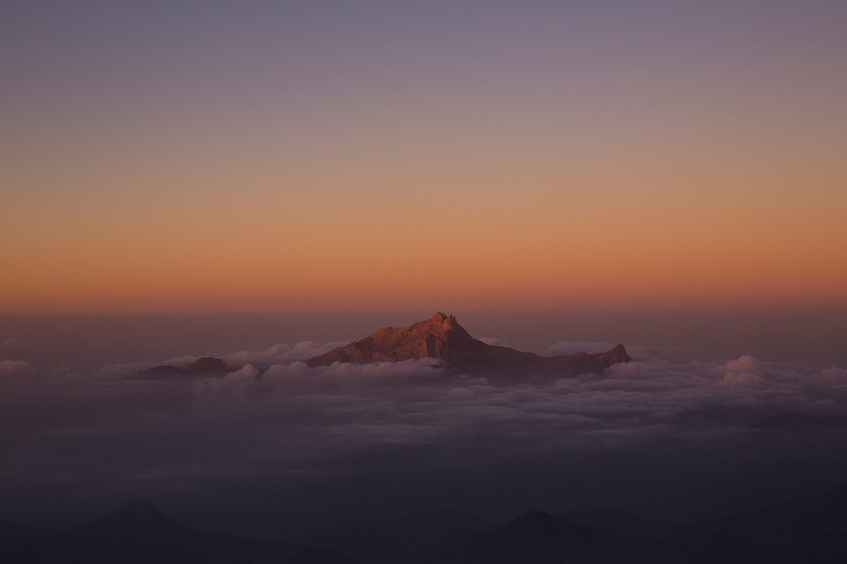 Mountain poking through clouds at sunset