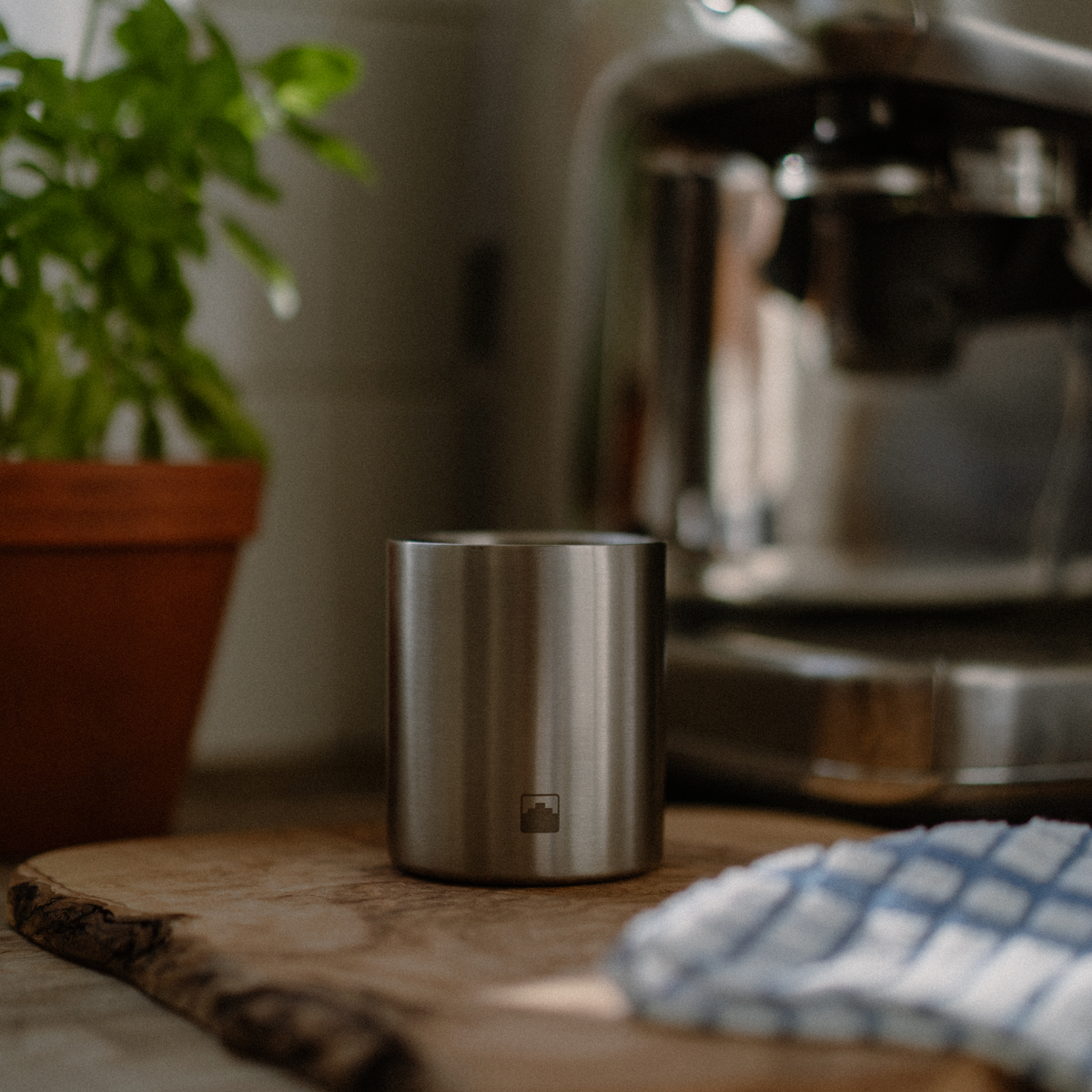 Stainless steel Babel candle on a wooden surface with a blurred coffee machine in the background